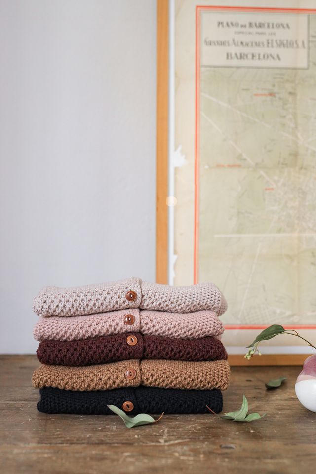 Stack of knitted sweaters on a wooden surface with a map in the background